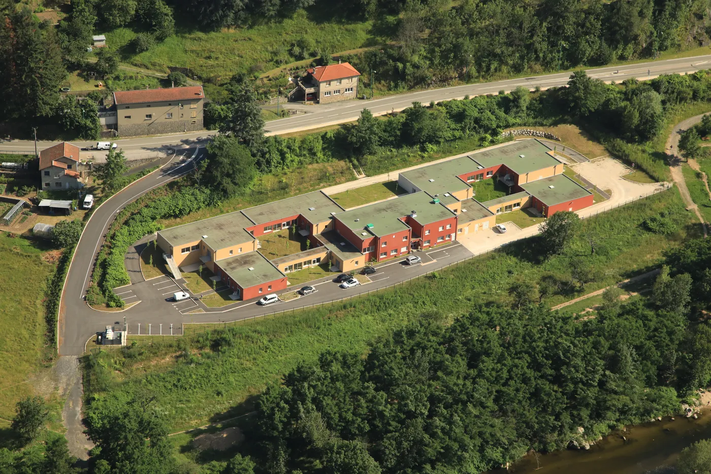 Vue aérienne de la résidence, de son parking et de la route qui serpente dans la vallée