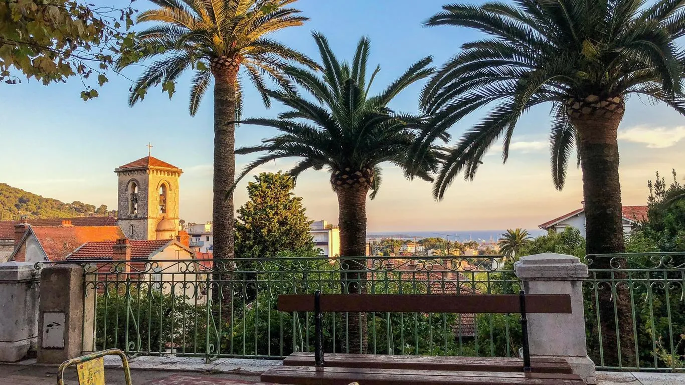Des palmiers et un banc sur une terrasse dominant les toits du Cannet au coucher du soleil