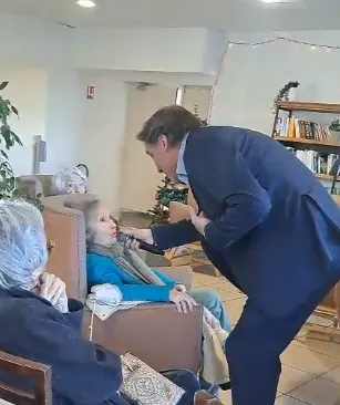Un chanteur en costume bleu se penche pour saluer une résidente dans son fauteuil