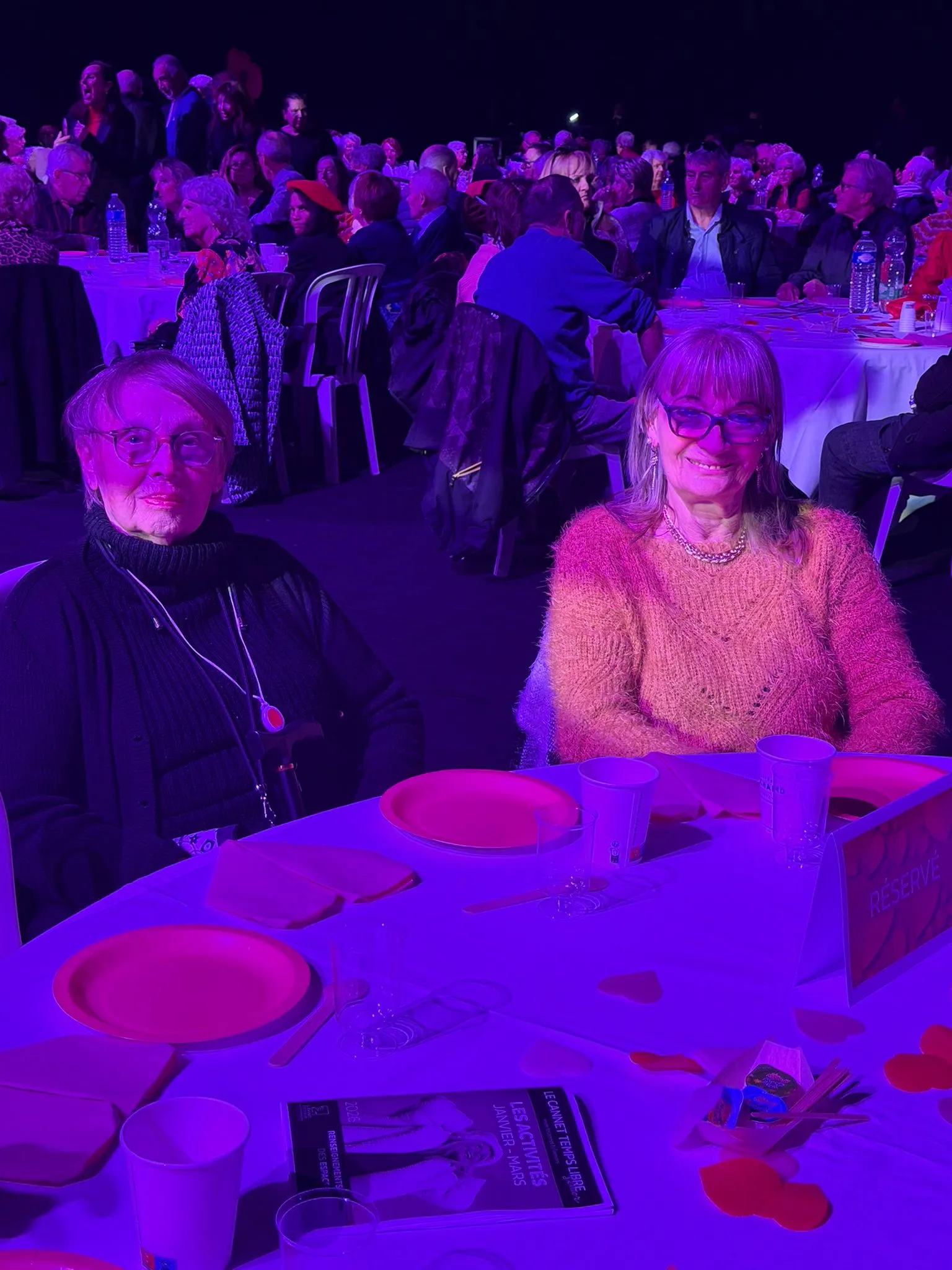 Deux résidentes souriantes attablées lors de la soirée de la Saint-Valentin au Cannet, salle décorée de cœurs