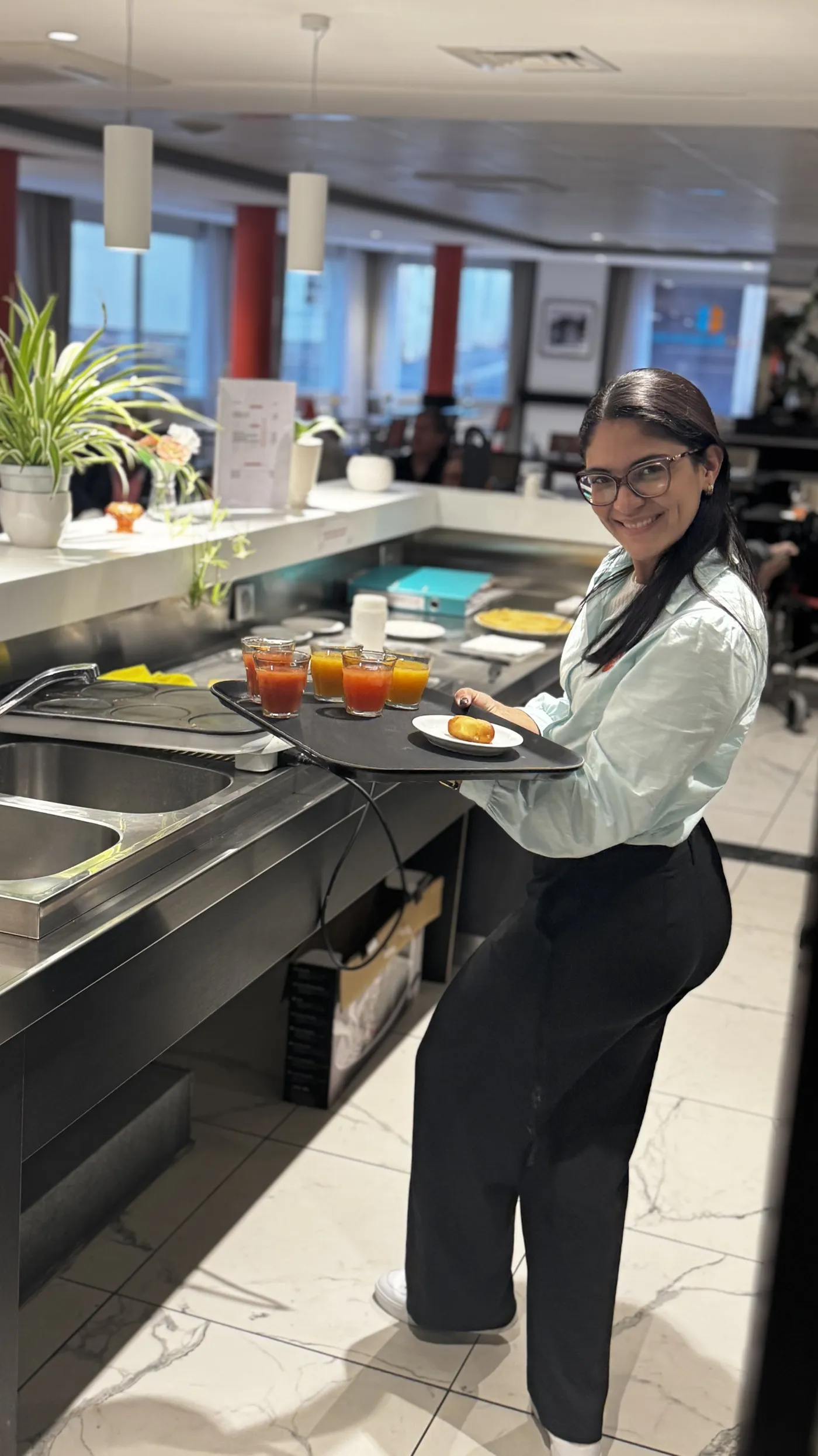 Une serveuse porte un plateau de jus de fruits près du comptoir du restaurant