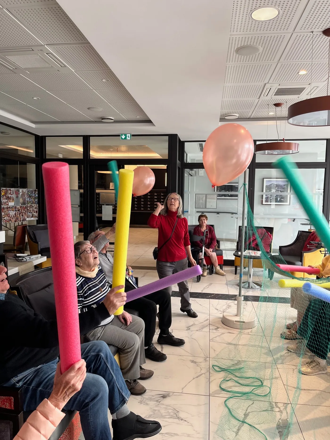 Des résidents assis en cercle brandissent des frites de piscine colorées pendant un jeu d'exercice