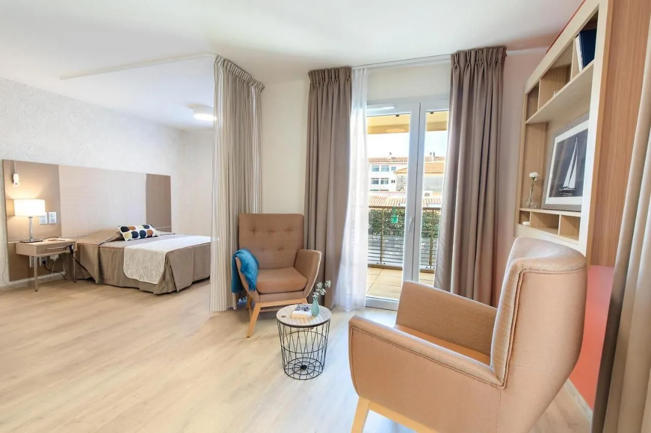 Furnished apartment at the OBEO Fréjus residence: sleeping area behind a curtain, two armchairs around a coffee table and French windows opening onto a balcony.