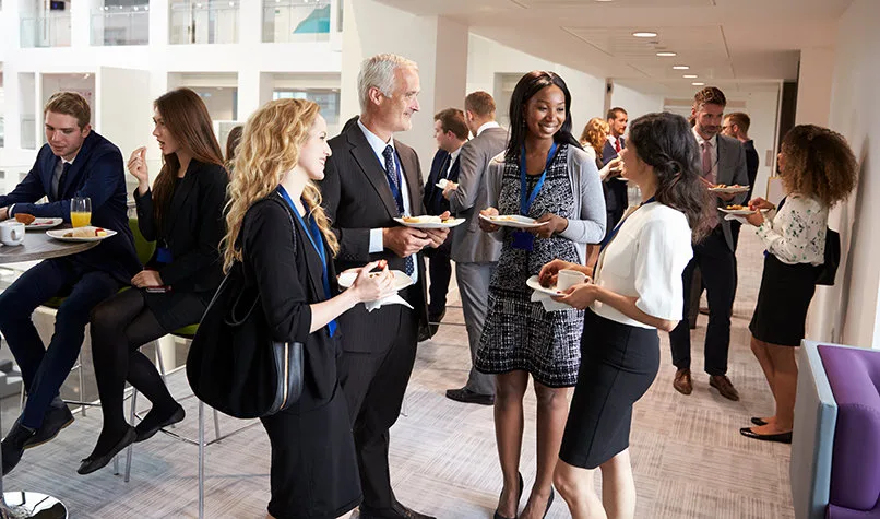 Professionals in business dress talking in a bright hallway, name badges around their necks.