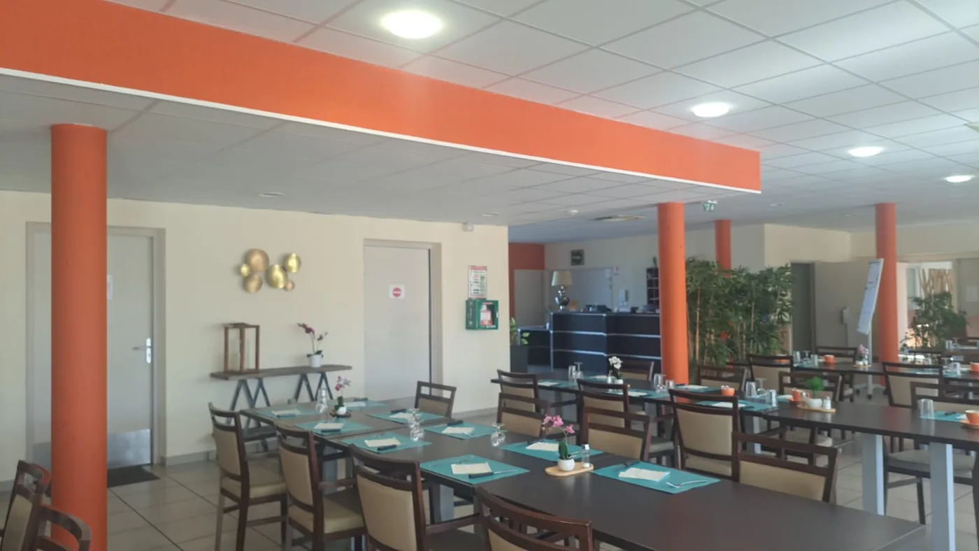 Une salle de restaurant vide, tables dressées sous un long bandeau de plafond orange