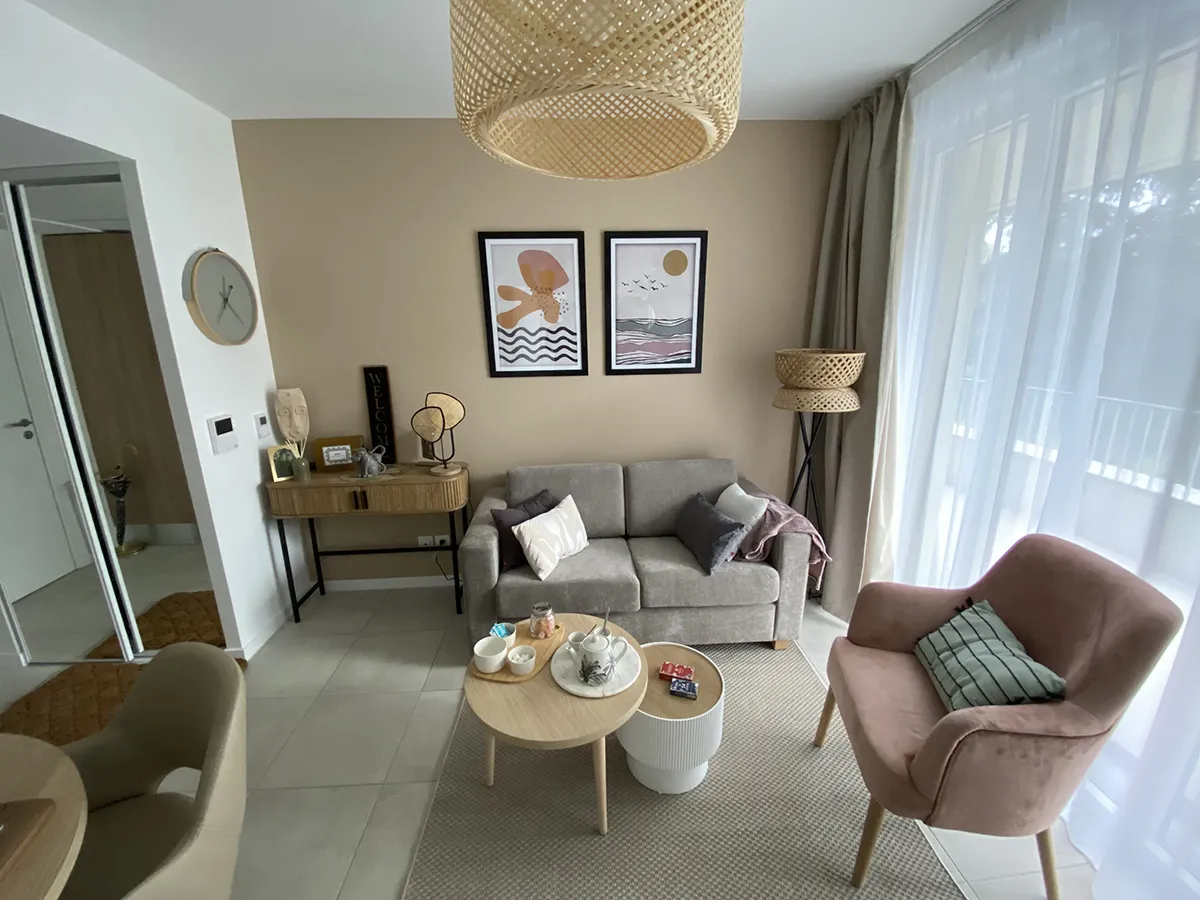 Living area of a show apartment in Toulouse-Guillaumet: grey sofa, pink armchair, round coffee tables and a large sheer-curtained window
