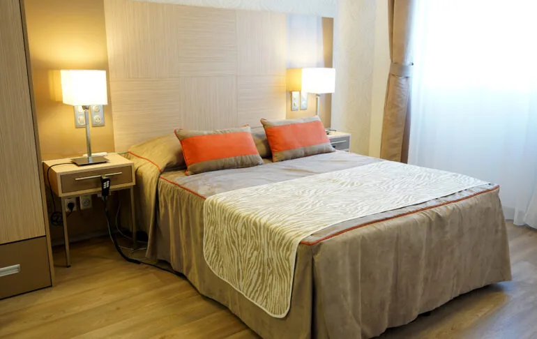 Bedroom of a show apartment in Uzès: double bed, wall reading lights and bedside tables in front of a bright sheer curtain